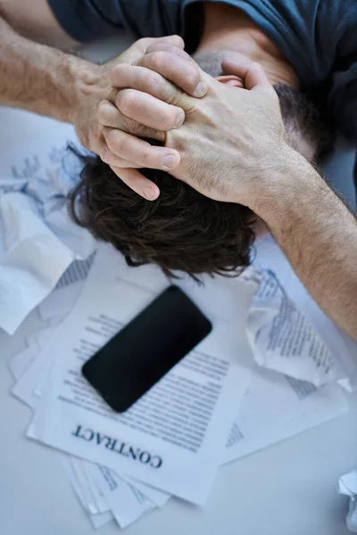 Vista superior do homem deprimido com smartphone com papéis e contrato perto dele durante colapso mental — Fotografia de Stock