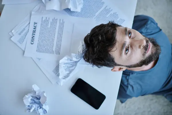 Blick von oben auf depressiven Mann mit Smartphone mit Papieren und Vertrag in seiner Nähe während eines Nervenzusammenbruchs — Stockfoto