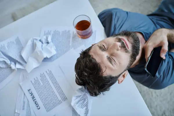 Vista superior del hombre deprimido con smartphone con vaso de alcohol a su lado durante la crisis mental - foto de stock