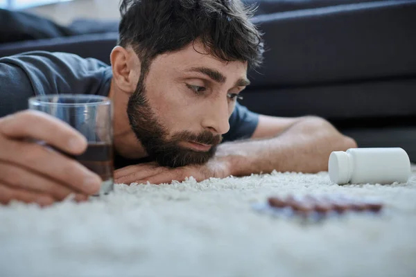 Depressed man in casual attire drinking alcohol and looking at pills during mental breakdown — Stock Photo