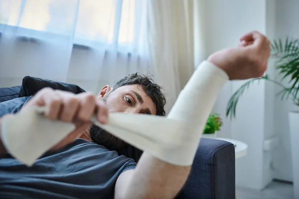 Травмированный мужчина с бинтом на руке после попытки самоубийства лежа на диване, психического здоровья осведомленности — стоковое фото