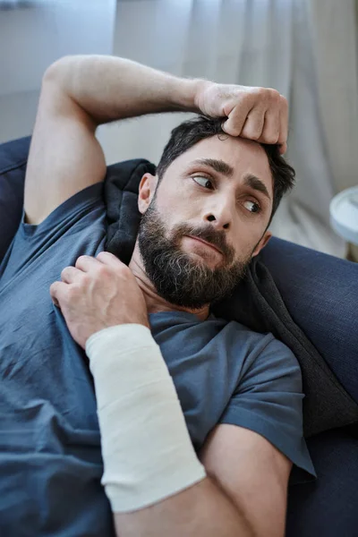 Отчаянный человек с повязкой на руке после попытки самоубийства лежа на диване, психического здоровья осведомленности — стоковое фото
