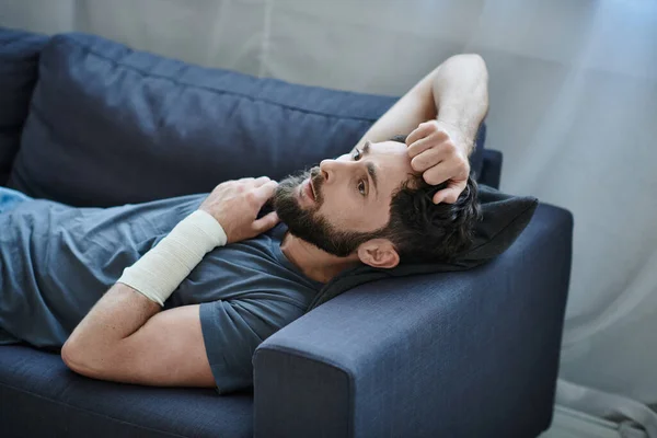 Hombre desesperado con vendaje en el brazo después de intentar suicidarse acostado en el sofá, conciencia de salud mental - foto de stock