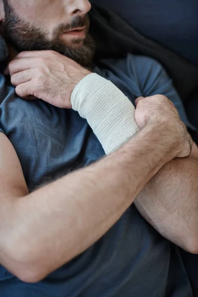 Vista recortada del hombre deprimido con vendaje en el brazo después de intentar suicidarse, conciencia de salud mental - foto de stock