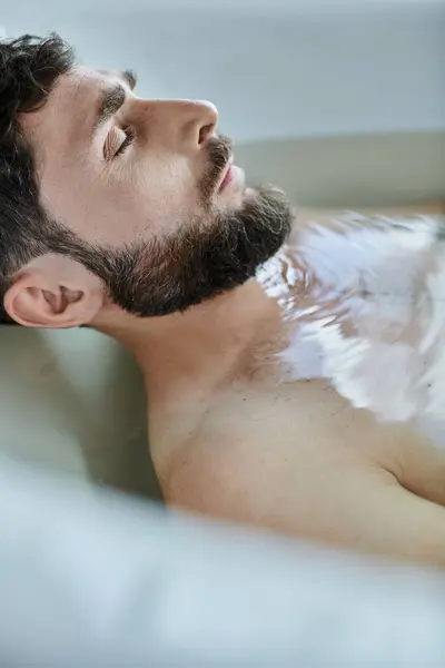 Hombre traumatizado deprimido con barba acostado en la bañera durante la ruptura, conciencia de salud mental - foto de stock