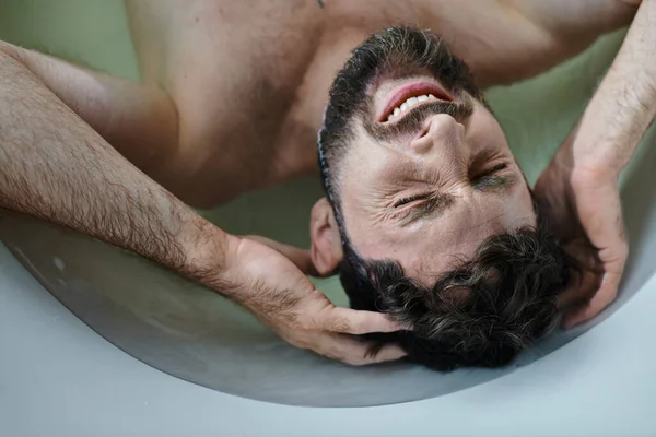 Angustioso hombre traumatizado acostado en la bañera y llorando durante el colapso, conciencia de salud mental - foto de stock