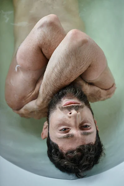 Больной травмированный мужчина с бородой, лежащий в ванной во время нервного срыва, осознание психического здоровья — стоковое фото