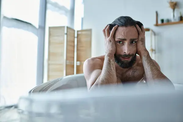 Hombre desesperado con barba sentado en la bañera con las manos en la cabeza durante la crisis mental, depresión - foto de stock