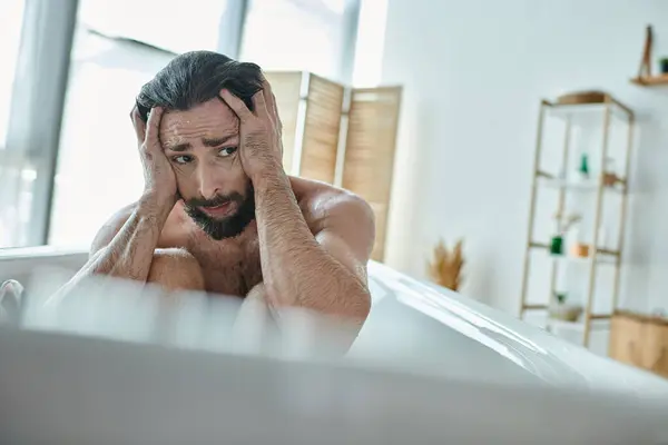 Отчаянный человек с бородой сидит в ванной с руками на голове во время психического срыва, депрессии — стоковое фото