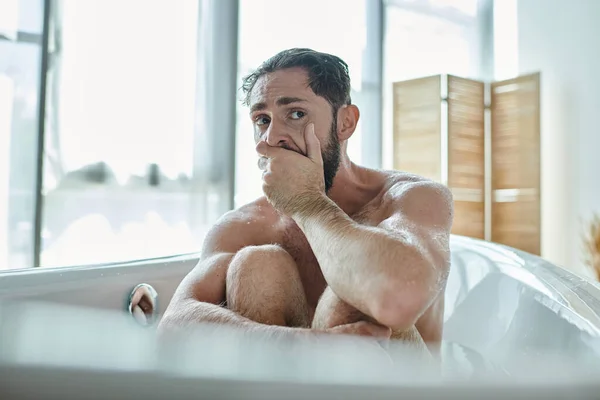 Hombre ansioso sentado en la bañera con las manos cerca de la cara durante el colapso, conciencia de salud mental - foto de stock