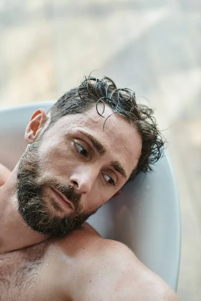 Hombre frustrado traumatizado con barba acostado en la bañera durante la ruptura, conciencia de salud mental - foto de stock