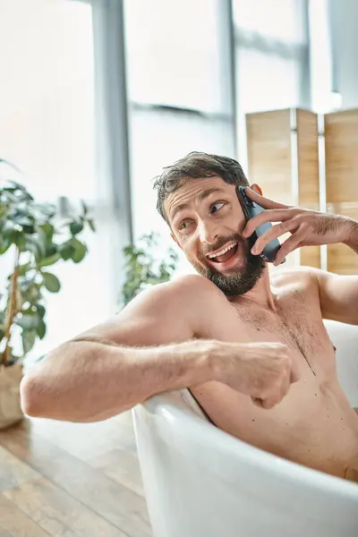 Alegre homem bonito com barba falando por telefone enquanto relaxa na banheira, saúde mental — Fotografia de Stock