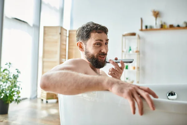 Allegro bell'uomo con la barba sdraiato nella vasca da bagno e registrare il messaggio audio, consapevolezza della salute mentale — Foto stock