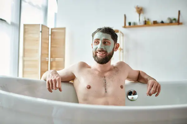 Joyous handsome man with beard and face mask chilling in his bathtub, mental health awareness — Stock Photo