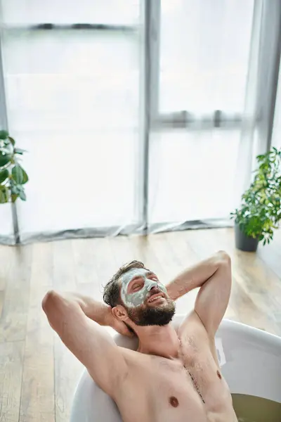 Good looking jolly man with beard and face mask chilling in his bathtub, mental health awareness — Stock Photo