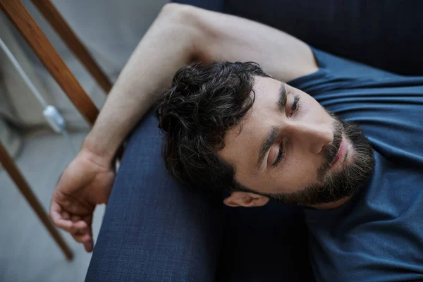 Depressiver ängstlicher Mann mit Bart in Freizeitkleidung, der während des Nervenzusammenbruchs auf dem Sofa liegt, Bewusstsein — Stockfoto