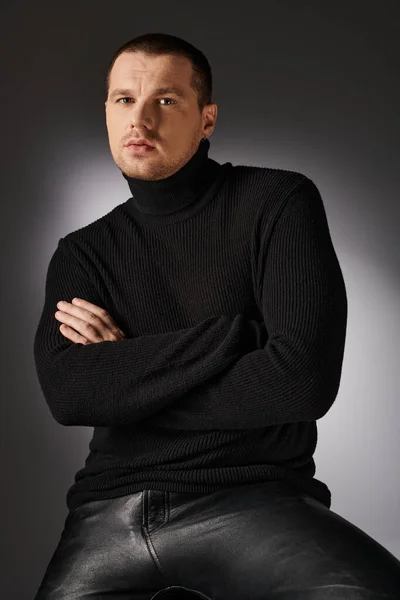 Pensive charismatic trendy man in black sweater looking at camera on grey backdrop with lighting — Stock Photo