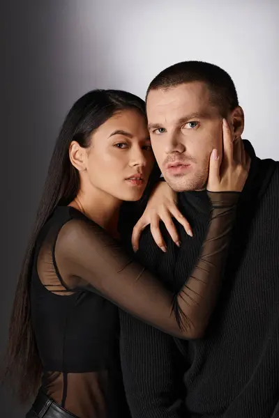 Elegant brunette asian woman in black stylish clothes hugging handsome man on grey backdrop — Stock Photo