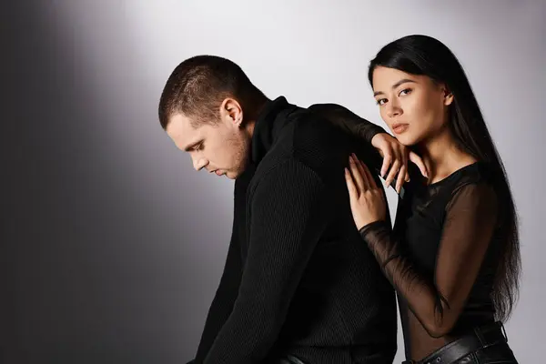 Charming asian woman leaning on man in black clothes and looking at camera on grey, love and fashion — Stock Photo