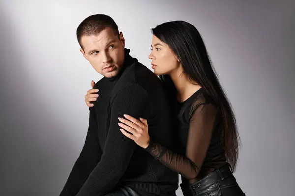 Young attractive asian woman hugging offended man sitting on grey backdrop, fashion and relationship — Stock Photo
