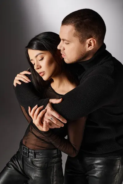 Handsome man in black outfit embracing alluring asian woman on grey backdrop, love and fashion — Stock Photo