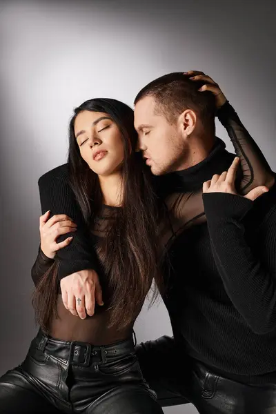 Trendy interracial couple in black casual attire embracing with closed eyes on grey backdrop — Stock Photo