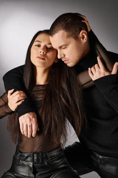 Seducente asiatico donna in nero vestiti guardando fotocamera vicino giovane uomo abbracciare lei su grigio — Foto stock