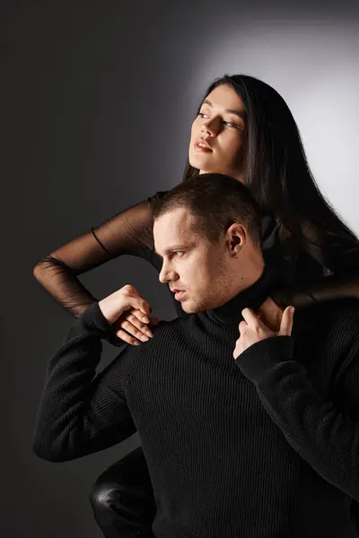 Alla moda coppia interrazziale in vestiti neri tenendosi per mano e guardando lontano su sfondo grigio — Foto stock