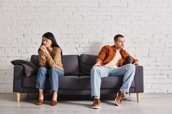 Deprimido interracial casal olhando embora enquanto sentado no sofá na sala de estar, divórcio conceito — Fotografia de Stock