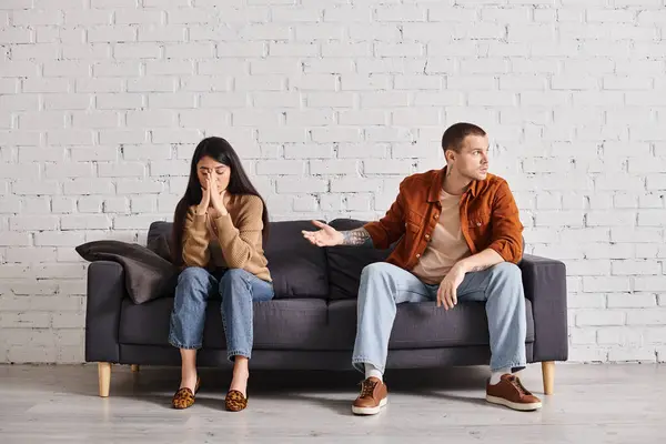 Scoraggiato uomo indicando offeso moglie asiatica sul divano in soggiorno, difficoltà di relazione — Foto stock