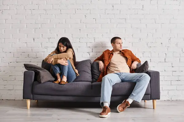 Offended asian wife looking at self-assured husband on couch in living room, misunderstanding — Stock Photo