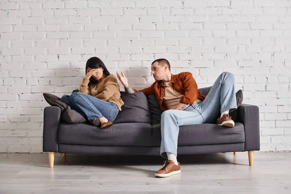 Young emotional man talking to asian woman crying on couch in living room, divorce concept — Stock Photo