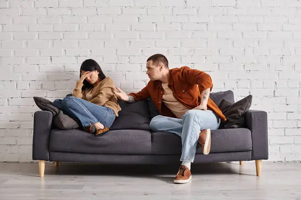 Junger irritierter Mann spricht mit junger asiatischer Frau, die auf Couch im Wohnzimmer weint, Scheidungskonzept — Stockfoto