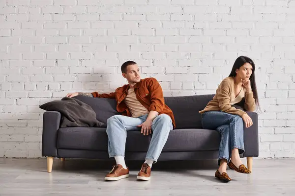 Giovane uomo guardando offeso asiatico moglie mentre seduta su divano in soggiorno, divorzio concetto — Foto stock