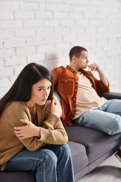 Jeune frustré asiatique femme assis avec les bras croisés près bouleversé mari sur canapé dans salon — Photo de stock