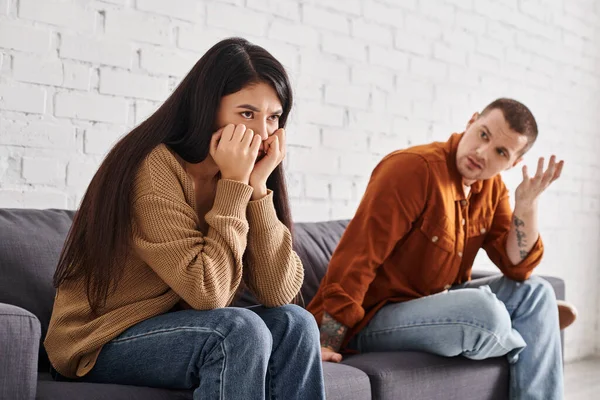 Scoraggiato uomo parlando con offeso asiatico moglie seduta su divano in soggiorno, divorzio concetto — Foto stock