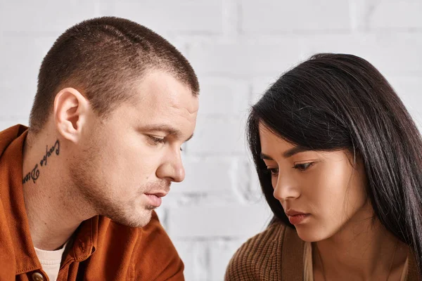 Joven y molesto pareja interracial hablando en la sala de estar en casa en casa, dificultades de relación - foto de stock