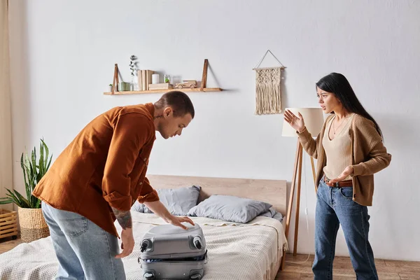 Angry asian woman quarreling at husband packing suitcase in bedroom, family divorce concept — Stock Photo