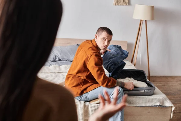 Offended tattooed man packing suitcase near wife quarreling in bedroom at home, divorce — Stock Photo