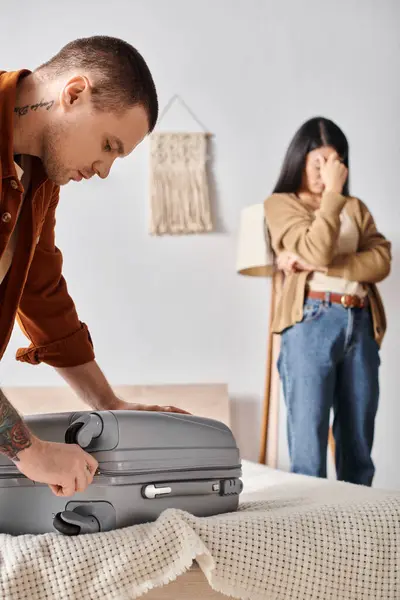 Joven hombre embalaje maleta cerca de deprimido asiático mujer llorando en dormitorio en casa, familia divorcio - foto de stock