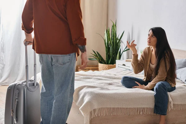 Chateado asiático mulher sentado no cama e falando no marido com mala em casa, divórcio conceito — Fotografia de Stock