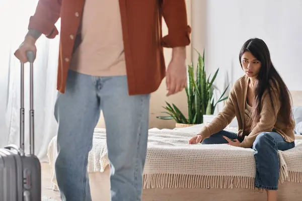 Depressed asian woman sitting on bed while her husband with suitcase leaving home, divorce — Stock Photo