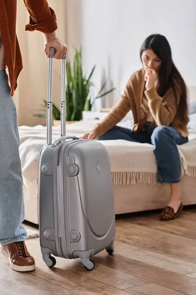 Frustrated asian woman sitting on bed while her husband with suitcase leaving home, divorce — Stock Photo