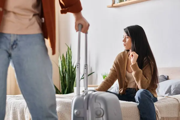 Jeune et triste asiatique femme assis sur lit tandis que son mari avec valise quitter la maison, divorce — Photo de stock