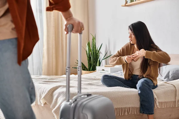 Offended asian woman taking off wedding ring while her husband with suitcase leaving home, divorce — Stock Photo