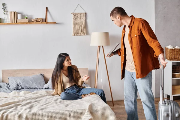 Homme avec valise et ordinateur portable querelle avec frustré asiatique femme dans chambre, concept de divorce — Photo de stock