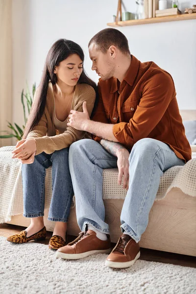 Giovane e tatuato uomo parlando con sconvolto asiatico moglie in camera da letto a casa, famiglia guai concetto — Foto stock