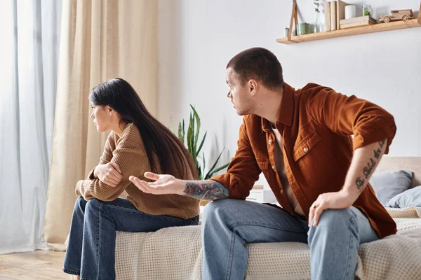 Wütend tätowierter Mann streitet über junge asiatische Frau weiß sitzt im Schlafzimmer zu Hause, Scheidungskonzept — Stockfoto