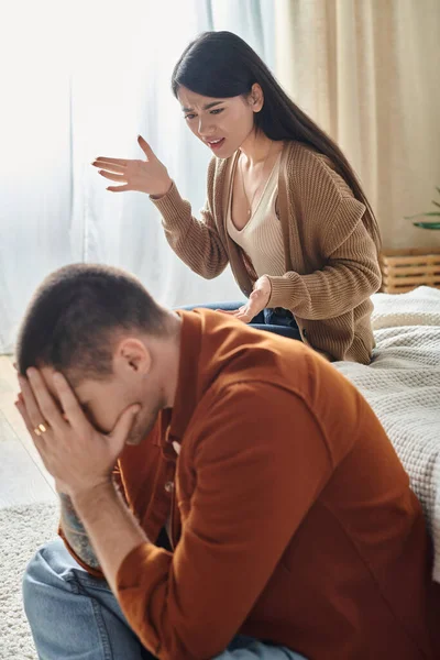 Angry asian woman quarrelling at husband sitting with bowed head on floor at home, divorce concept — Stock Photo