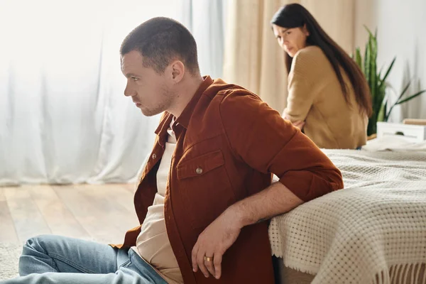 Junger frustrierter Mann sitzt auf dem Boden neben verärgerter asiatischer Frau, Beziehungsschwierigkeiten Konzept — Stockfoto